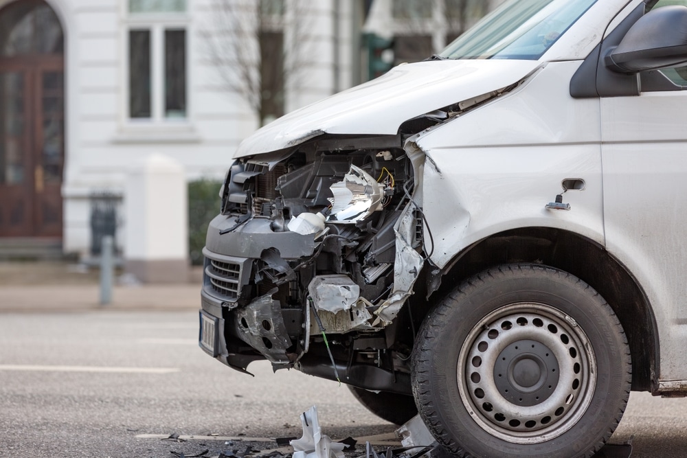 Close-up view of a white van with significant front-end damage after a collision.